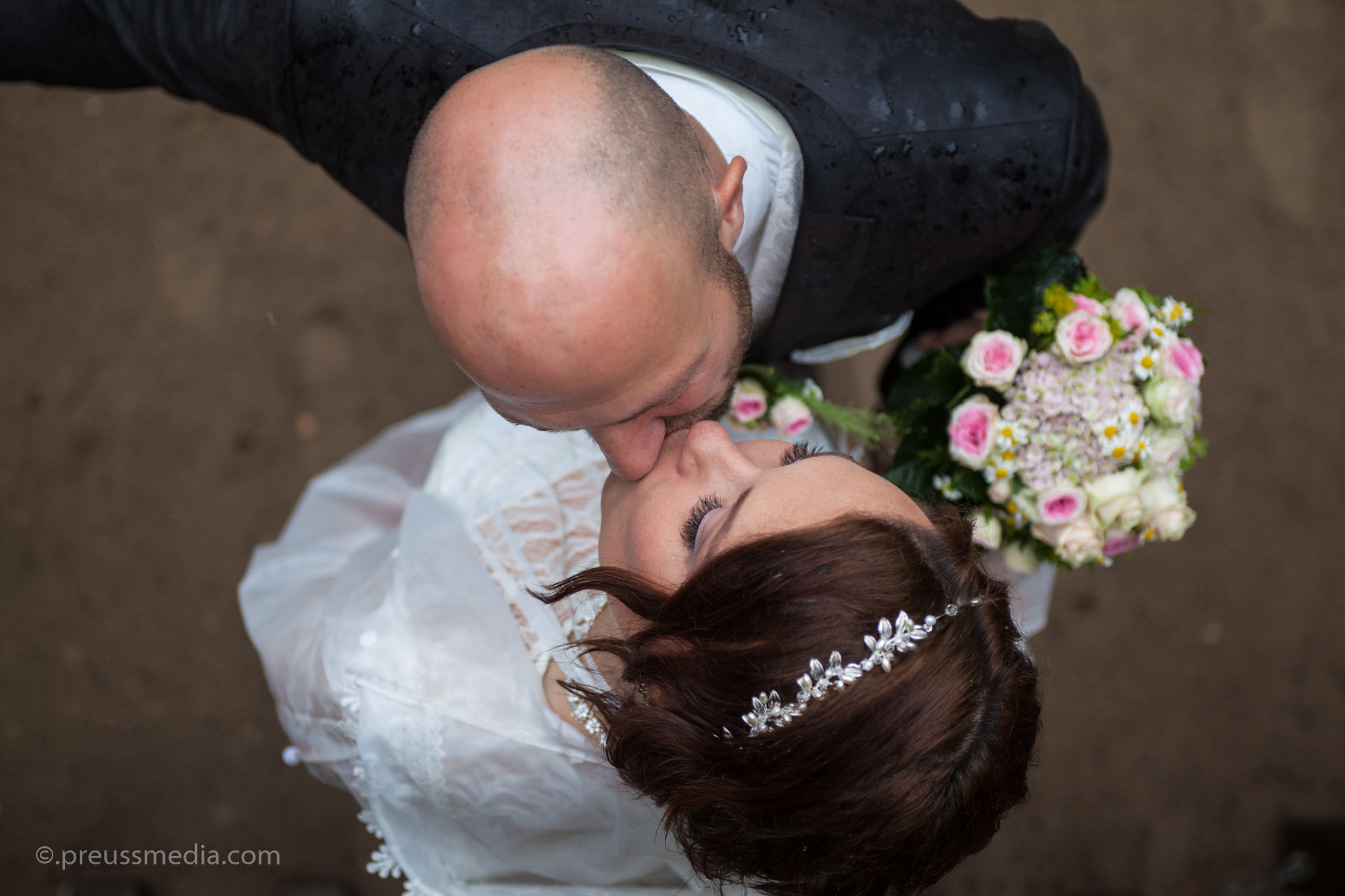 küssendes Brautpaar mit Blumenstrauss in Draufsicht