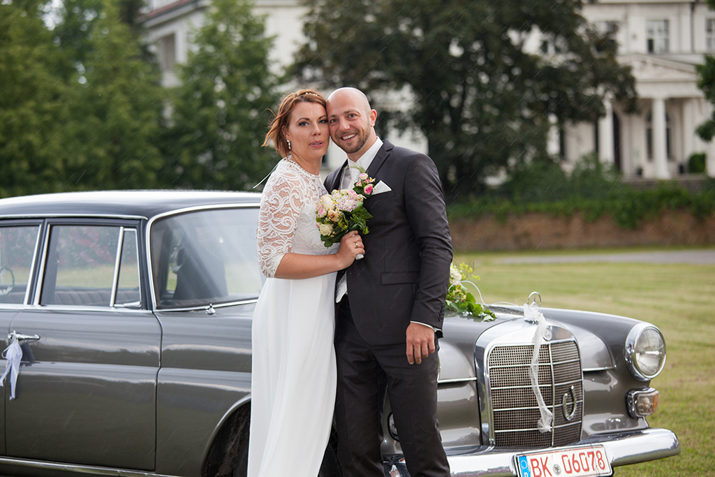 glückliches Brautpaar vor Brautauto mit Blumenschmuck